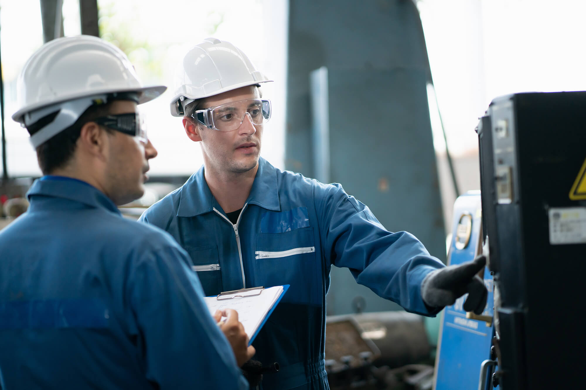 Manufacturing workers in hardhats discussing a piece of machinery equipment. Manufacturing workers in hardhats discussing a piece of machinery equipment.