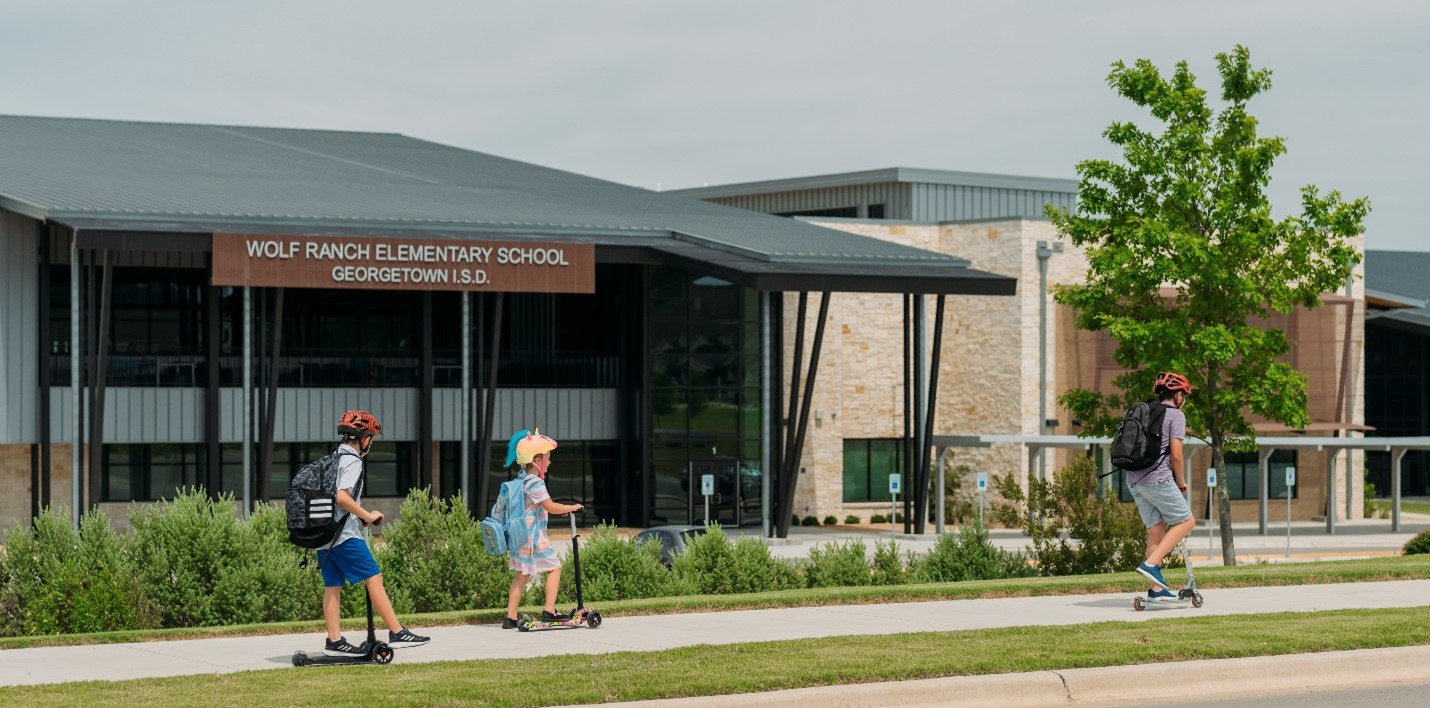 Schoolchildren riding scooters outside of Wolf Ranch Elementary School 